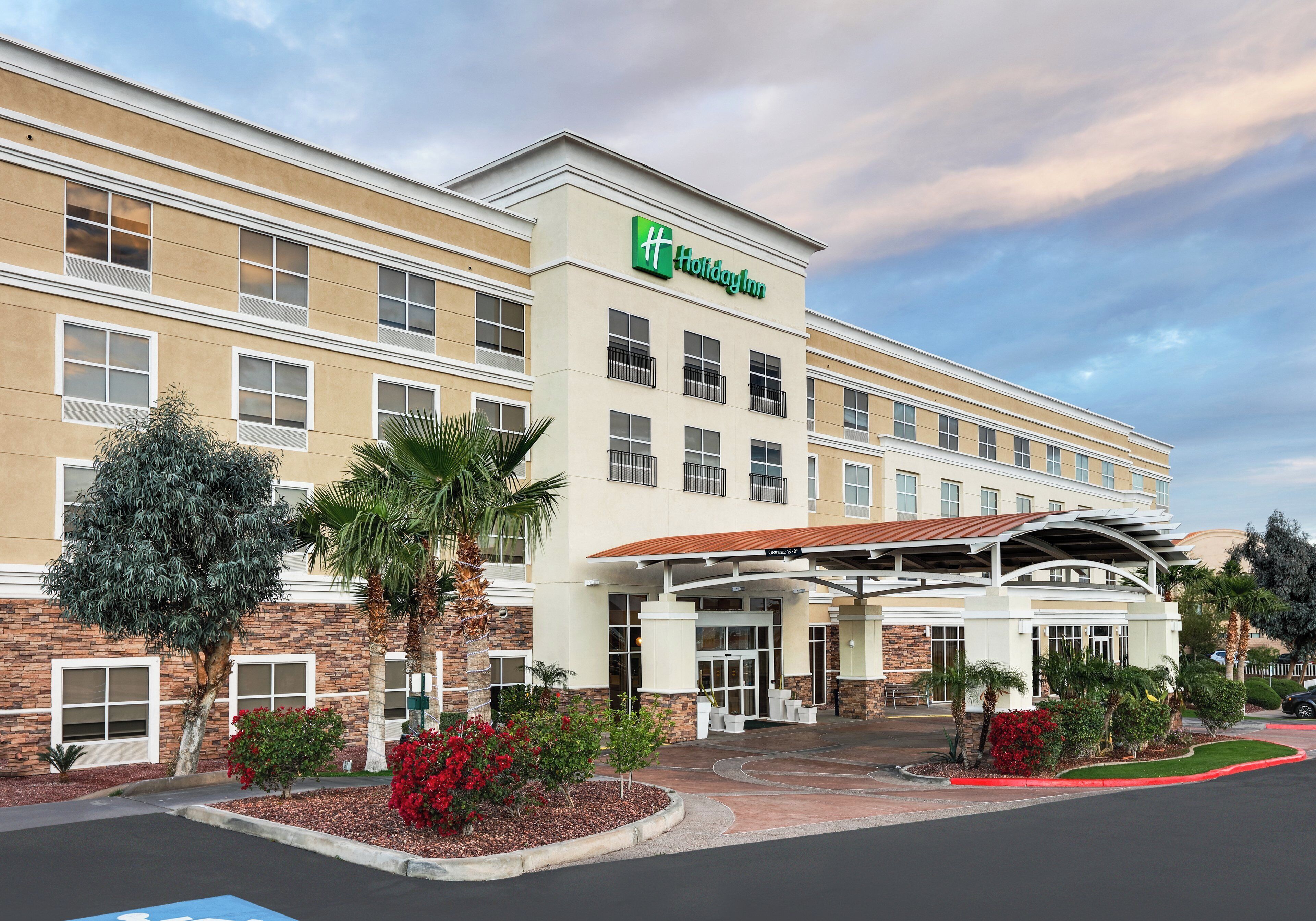 A Holiday Inn hotel with a covered entrance, multiple windows, and a landscaped front yard with trees and shrubs.
