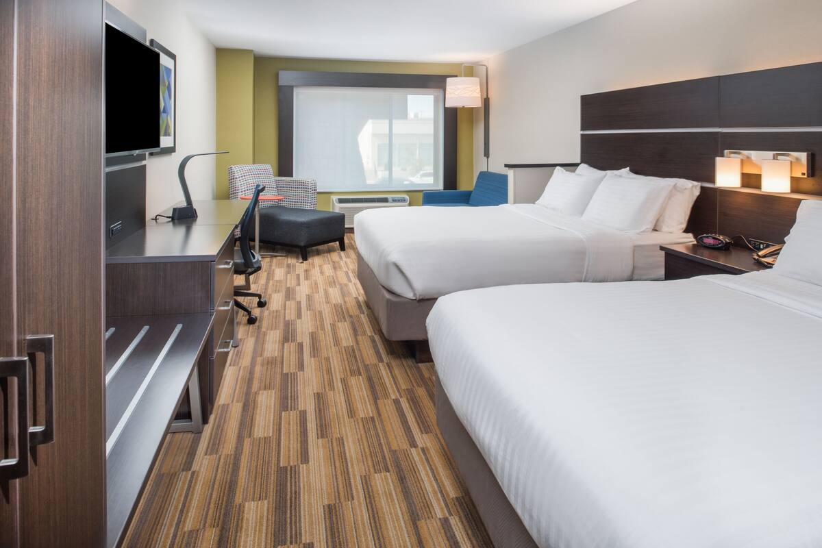 A hotel room with two beds, a desk, a chair, a TV, and a window with a view.