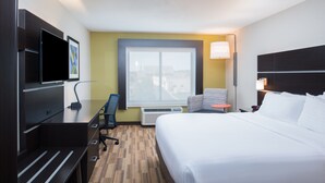 A hotel room with a large bed, a desk with a chair, a TV, a window, and an air conditioning unit. - Holiday Inn Express Hotel & Suites Bismarck by IHG (Bismarck)