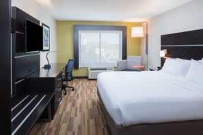 A hotel room with a large bed, a desk with a chair, a TV, a window, and an air conditioning unit. - Holiday Inn Express Hotel & Suites Bismarck by IHG (Bismarck)