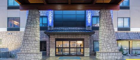 A building entrance with a stone facade, large windows, and a covered area with wooden beams.
