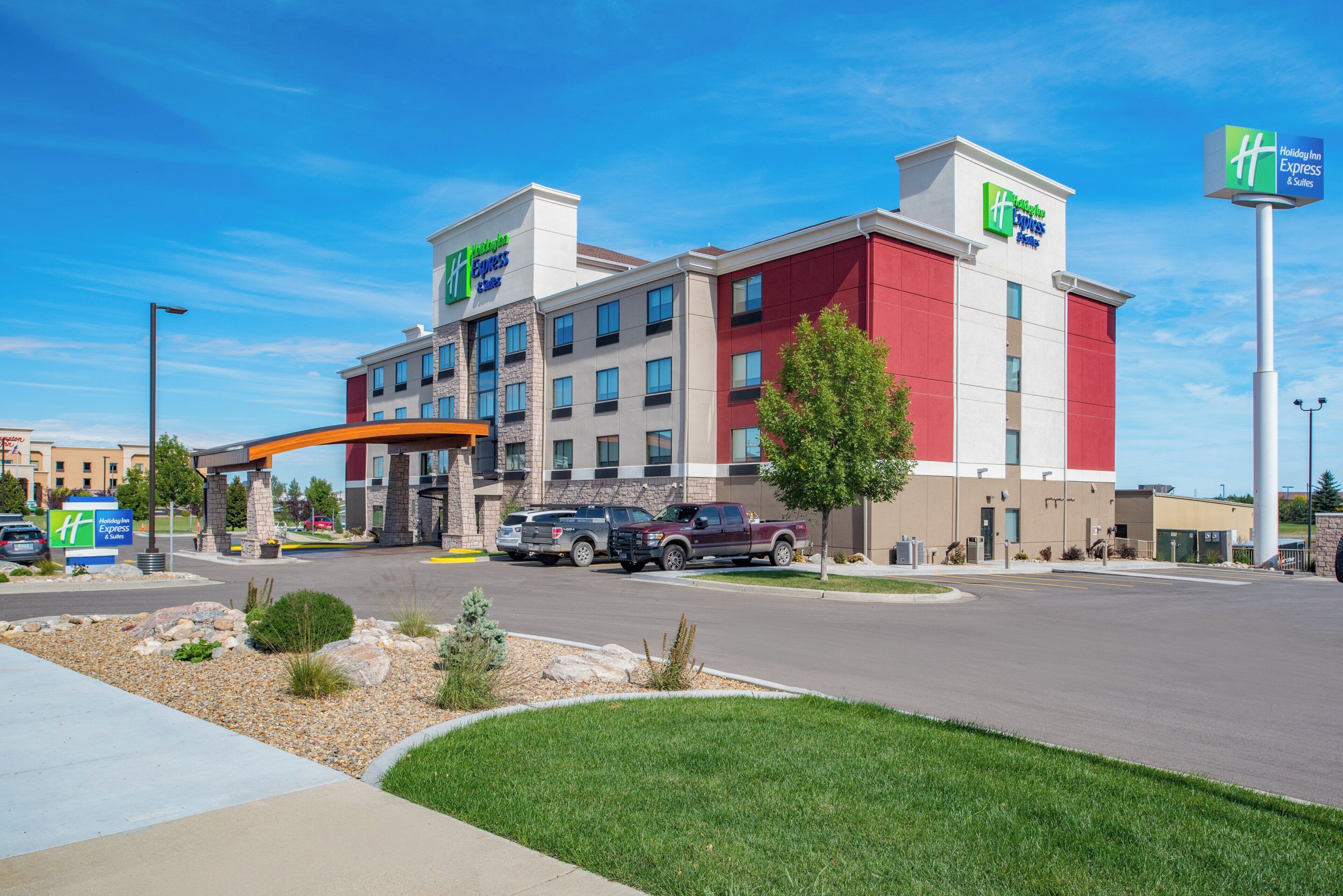 A Holiday Inn Express & Suites hotel with a modern design, featuring a prominent entrance, multiple parking spaces, and a well-maintained lawn area.
