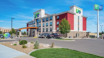 A Holiday Inn Express & Suites hotel with a modern design, featuring a prominent entrance, multiple parking spaces, and a well-maintained lawn area.