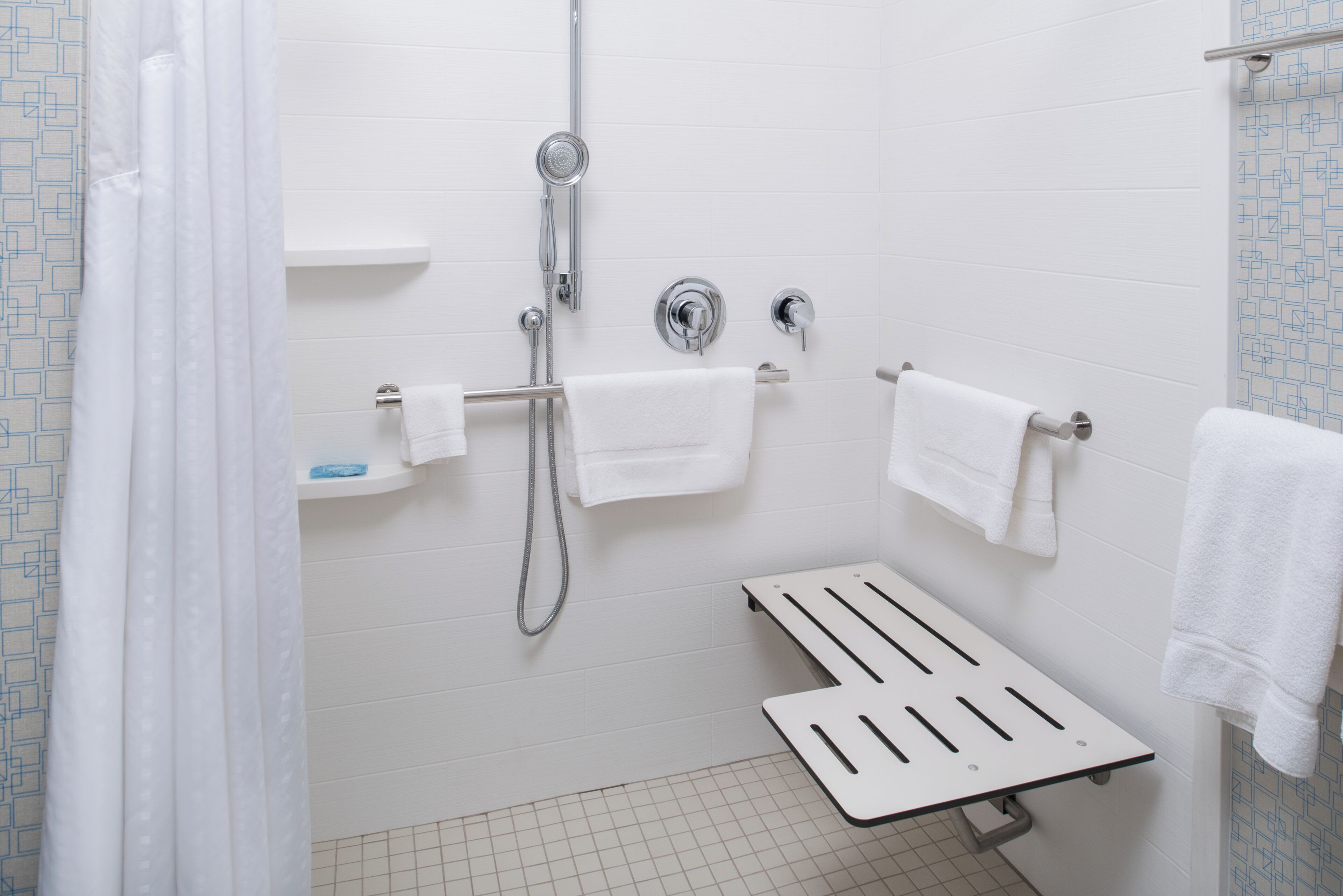 Een badkamer met witte betegelde wanden, een douche met handdouche en een toilet met een handdoekhouder.