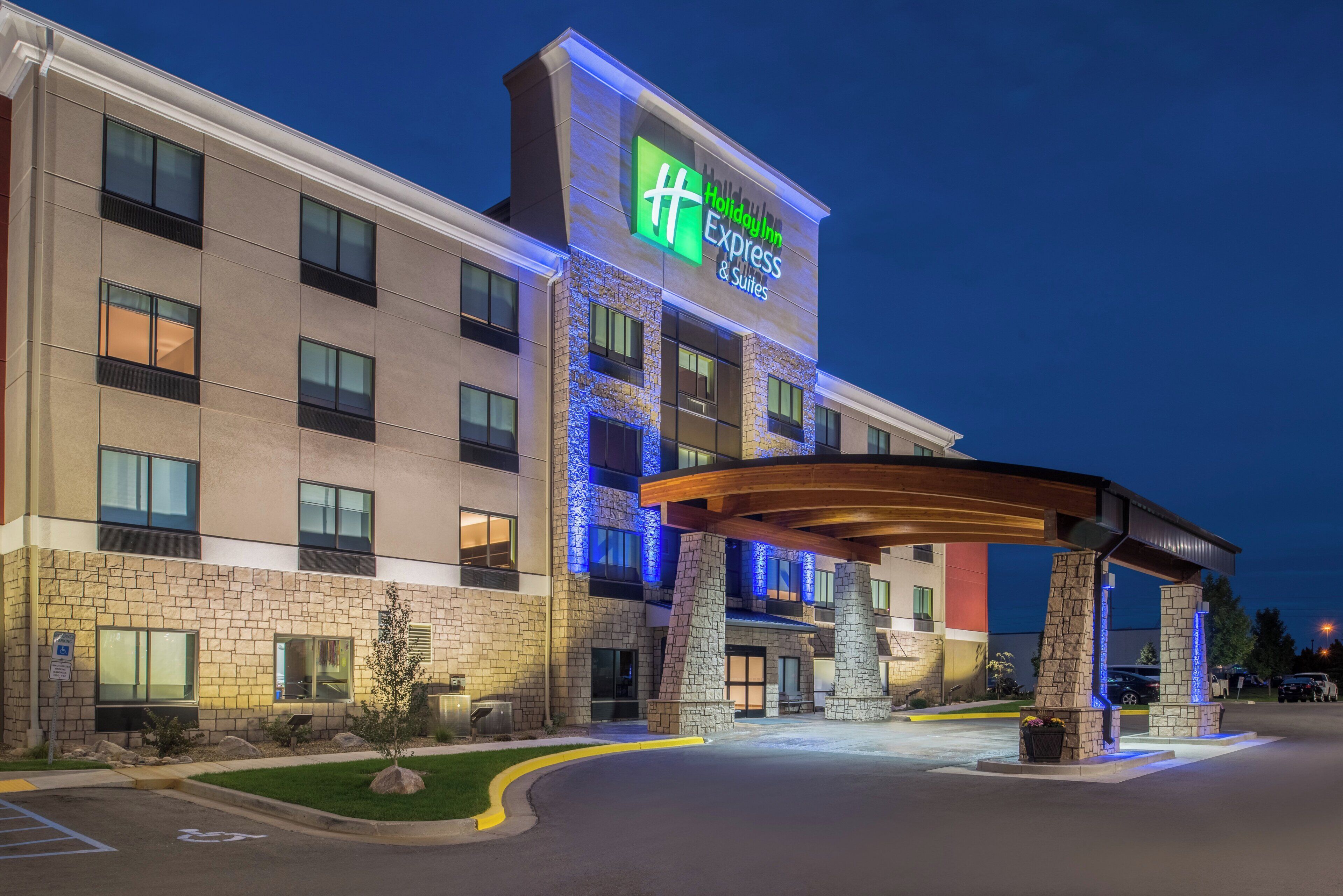 Un hotel Holiday Inn Express & Suites con fachada de piedra, un acceso cubierto y un estacionamiento.