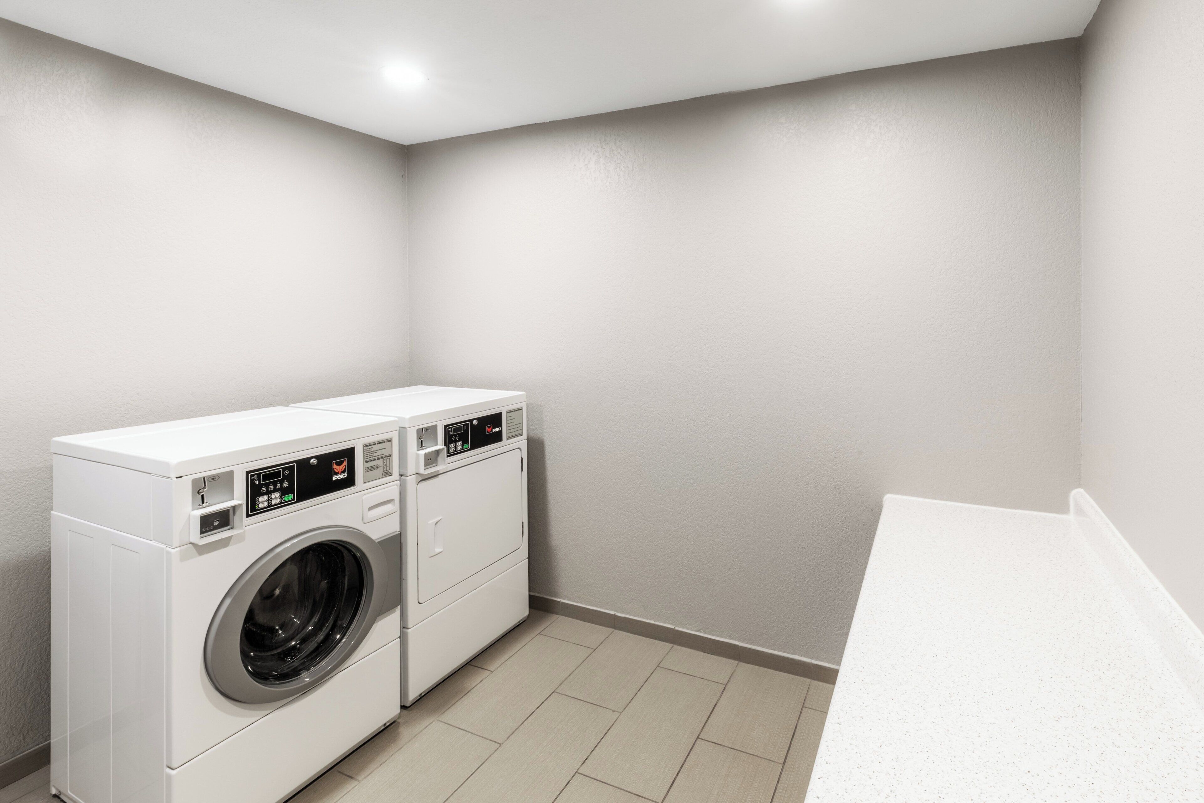 A laundry room with a front-loading washer and dryer, a countertop, and a tiled floor.