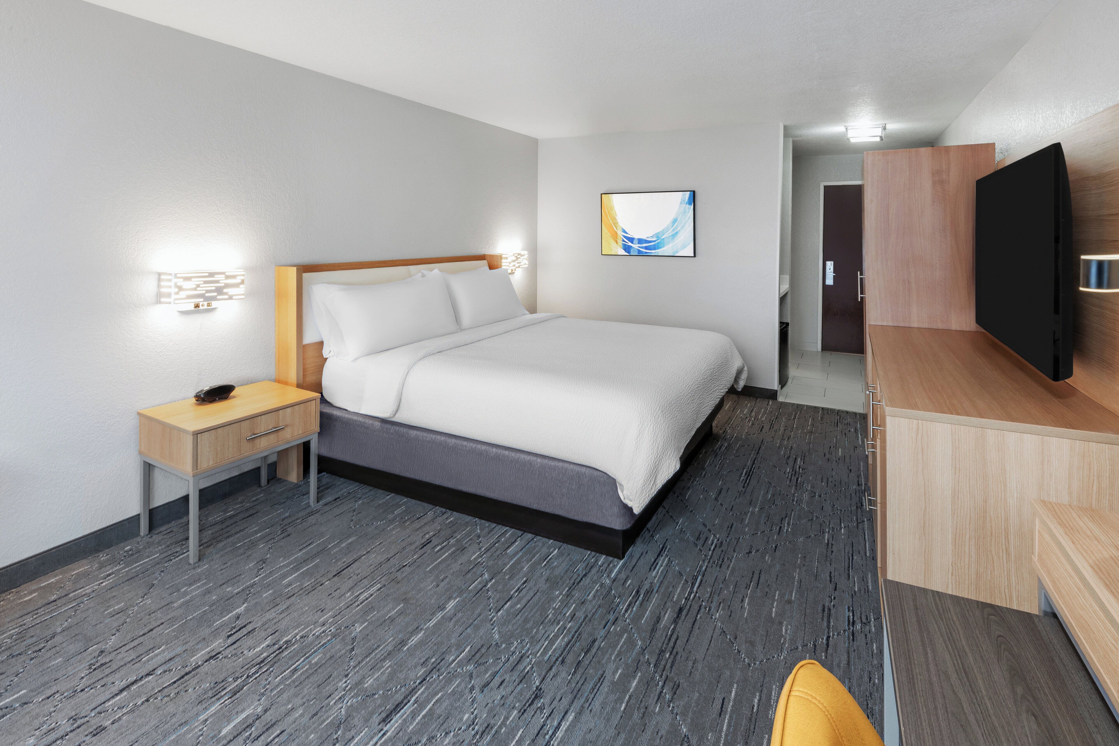 Una habitación de hotel moderna con cama, mesita de noche, televisor y escritorio con silla.