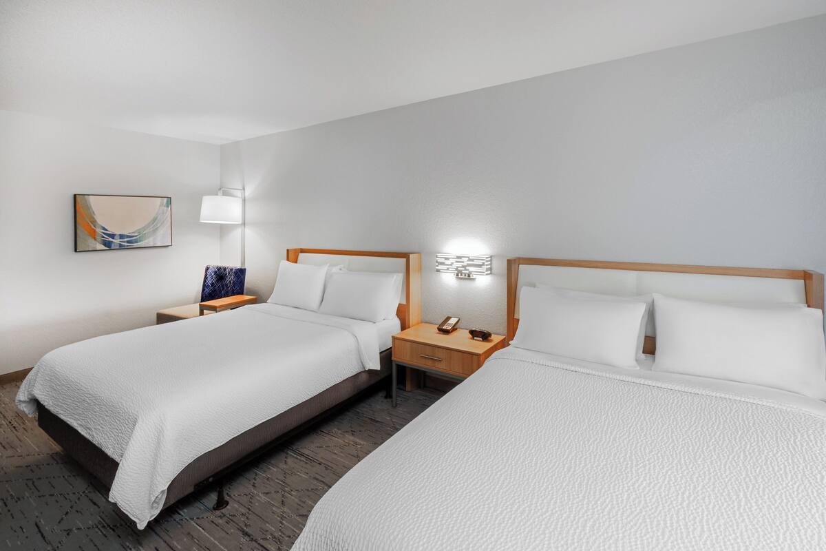 A hotel room with two beds, a nightstand with a lamp, and a wall-mounted artwork.