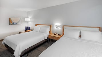 A hotel room with two beds, a nightstand with a lamp, and a wall-mounted artwork.