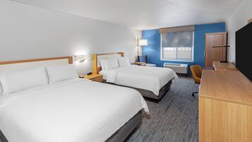 A hotel room with two beds, a desk, a chair, a wardrobe, and a window with blinds.