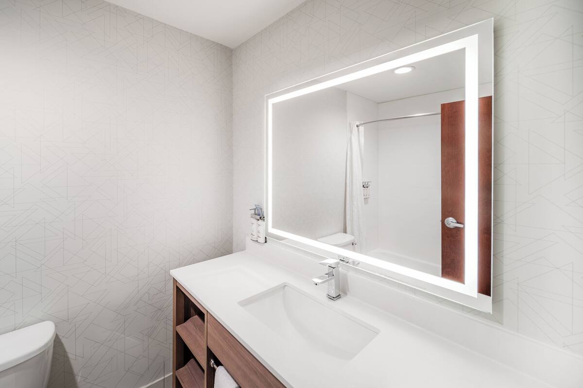 A modern bathroom with a large mirror, white sink, and wooden vanity.