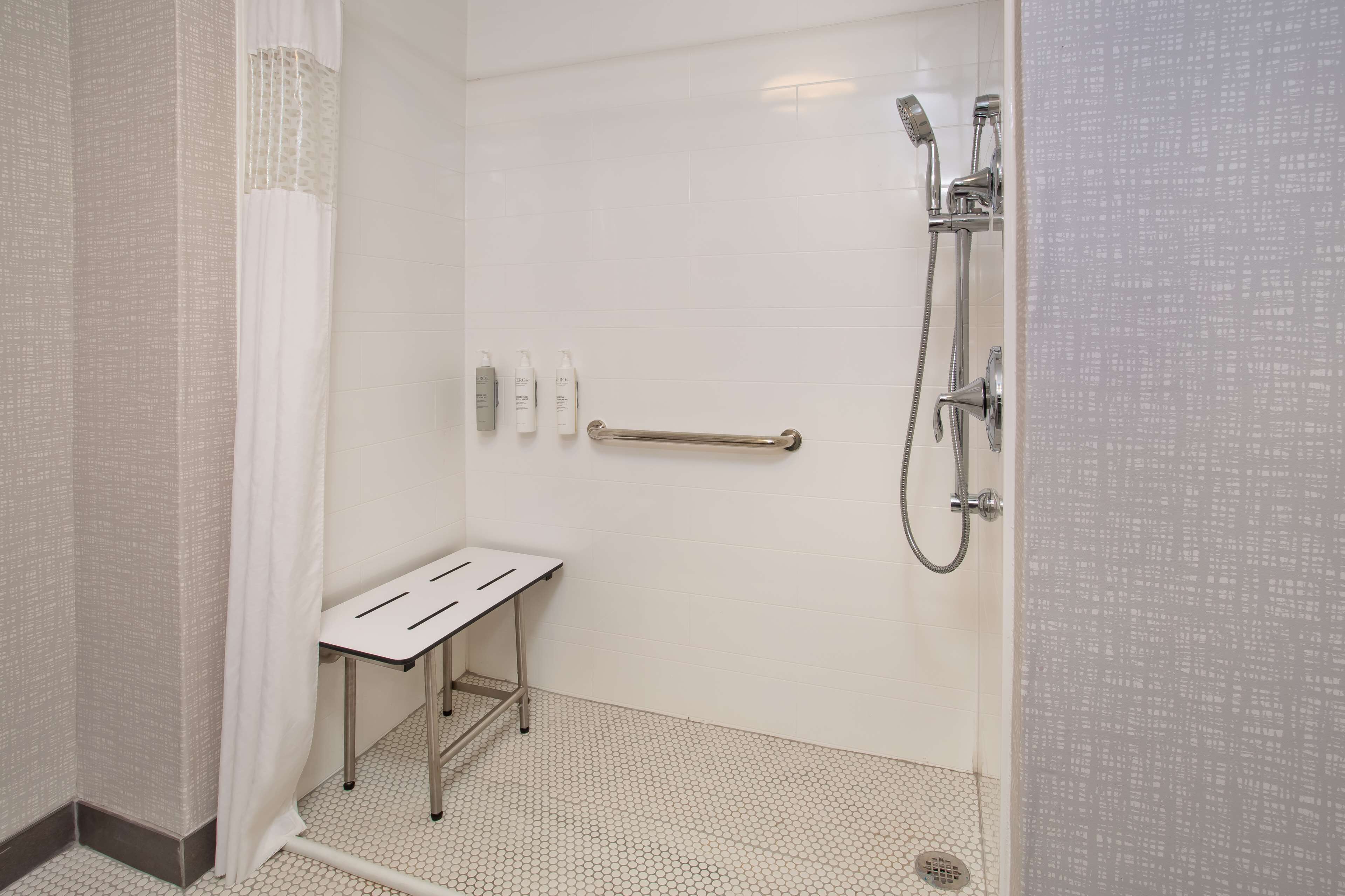 A shower area with a handheld showerhead, a handheld shower attachment, and a grab bar.