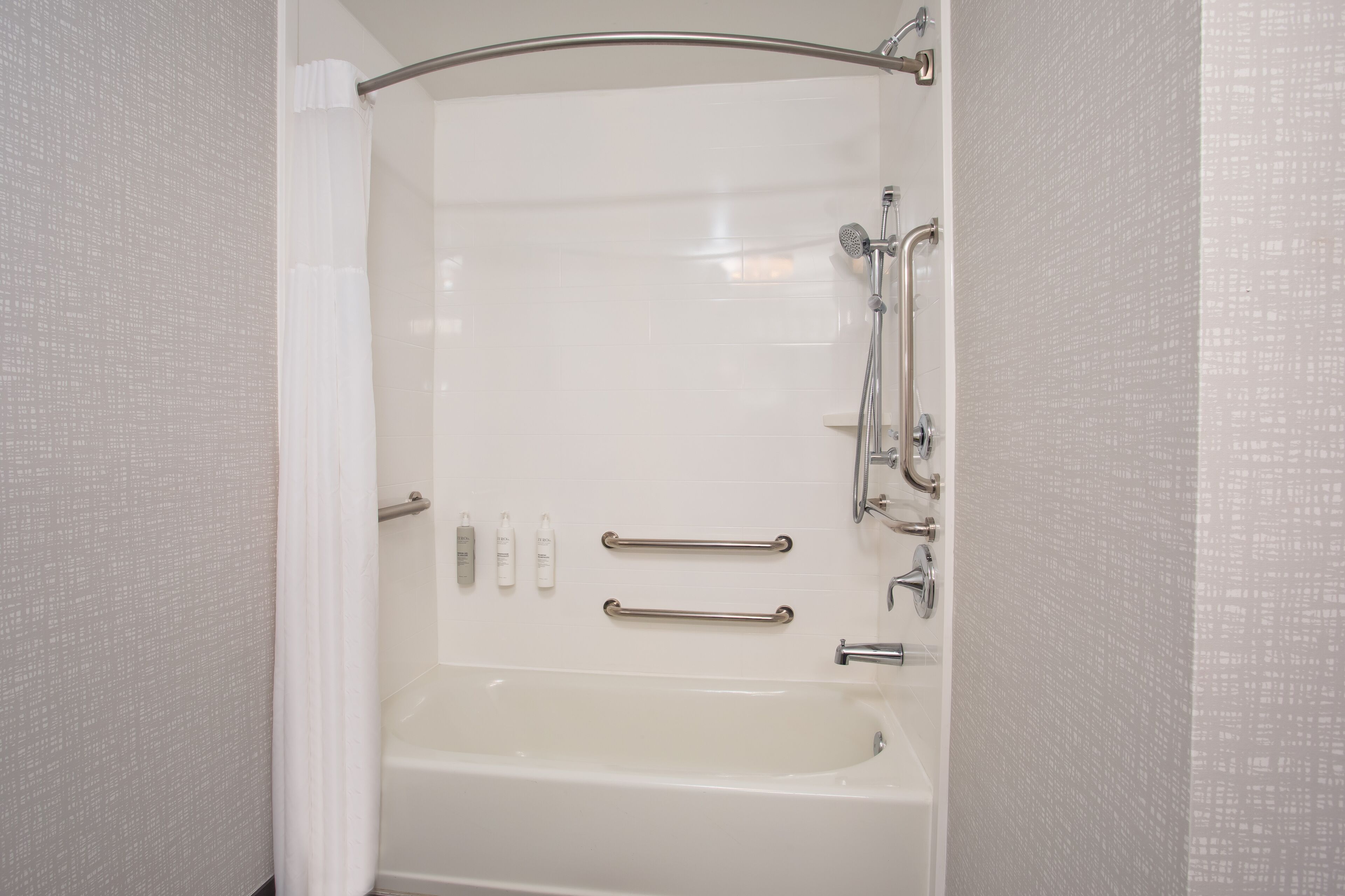 A walk-in shower with a glass door, grab bars, and a handheld showerhead.