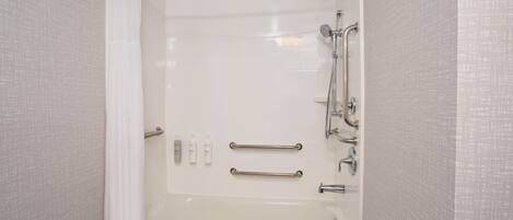 A walk-in shower with a glass door, grab bars, and a handheld showerhead.