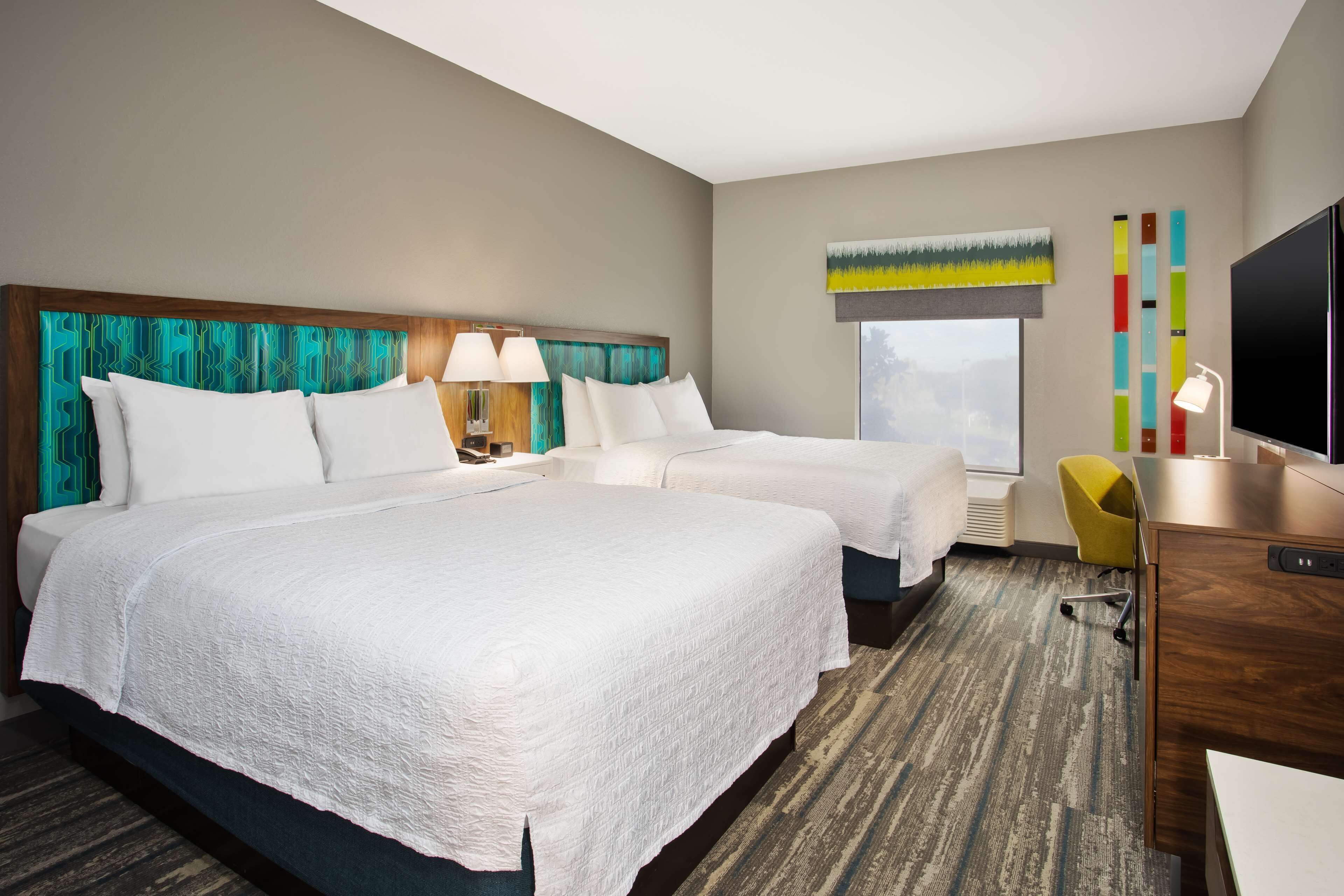 A hotel room with two beds, a desk, a TV, and a window with a view.