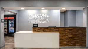 A reception area with a 'Welcome to the Sun Shine State' sign, a Hilton Honors logo, and a modern reception desk. - Hampton Inn & Suites Lady Lake/The Villages (Lady Lake)
