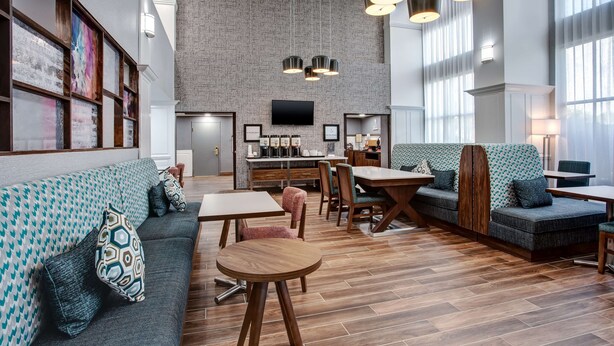 A modern lounge area with a brick wall, wooden flooring, and a mix of seating options including sofas and a small table. - Hampton Inn & Suites Lady Lake/The Villages (Lady Lake)