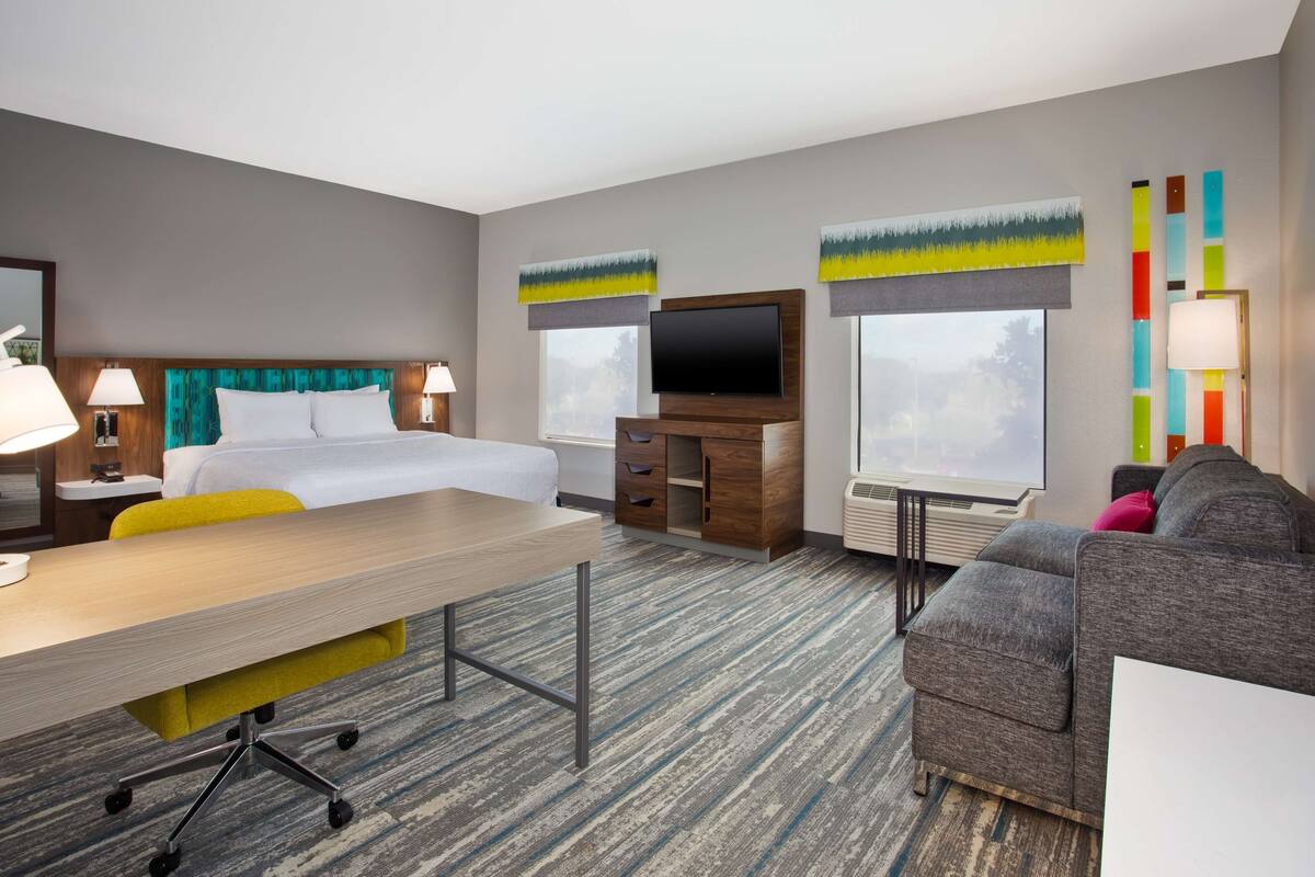 A hotel room with a bed, a desk, a TV, a sofa, and a window.