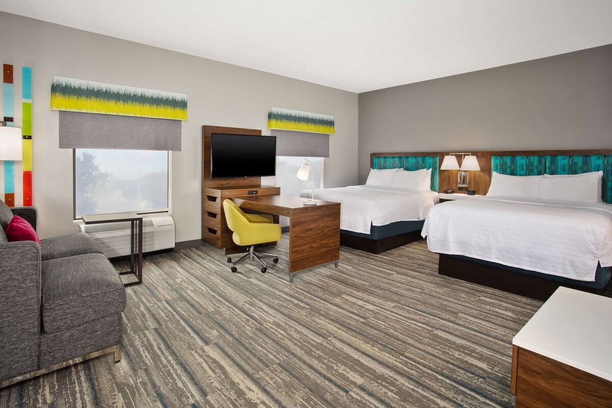 A hotel room with two beds, a desk with a chair, a TV, and a sofa.