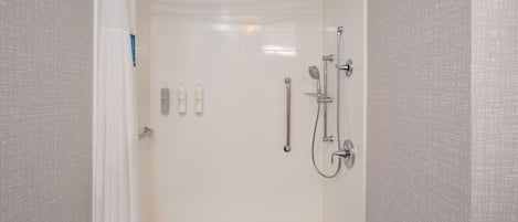Un espace douche moderne doté d’une porte en verre, d’un pommeau de douche à main, d’un robinet mural et de deux bouteilles de shampoing.