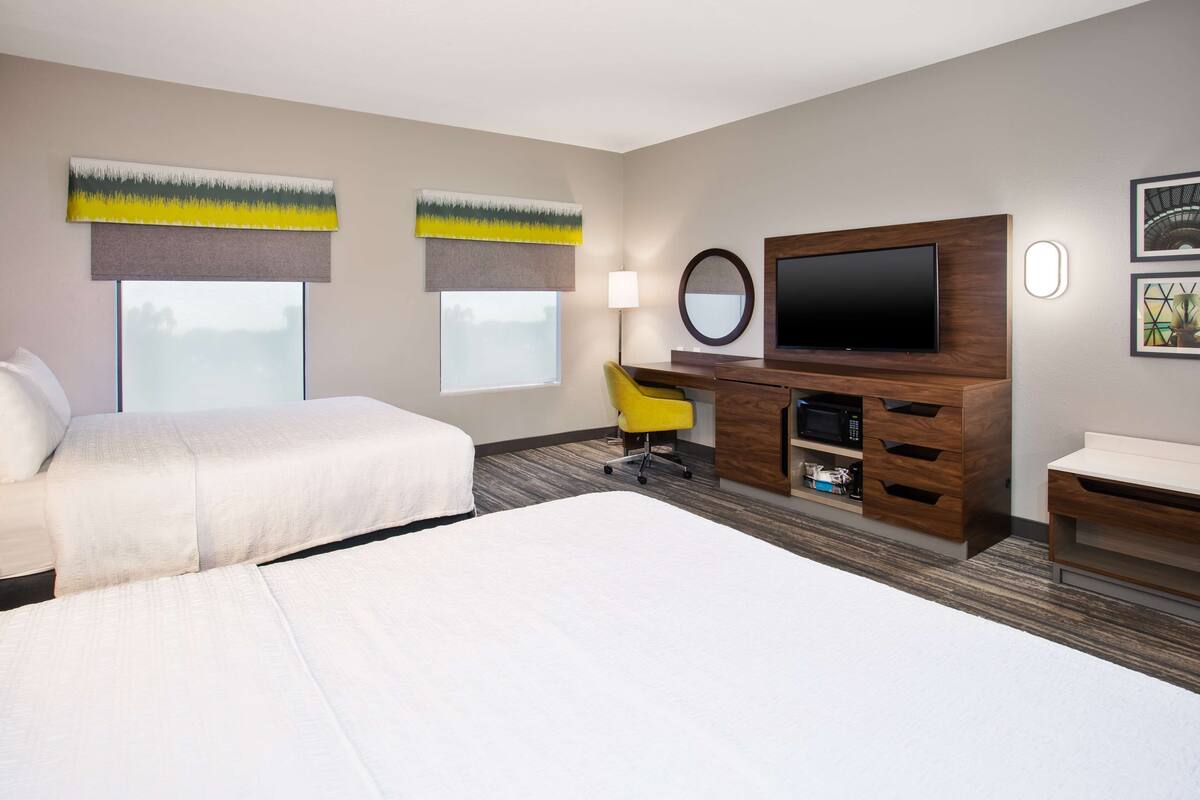 A hotel room with two beds, a desk, a TV, and artwork on the walls.