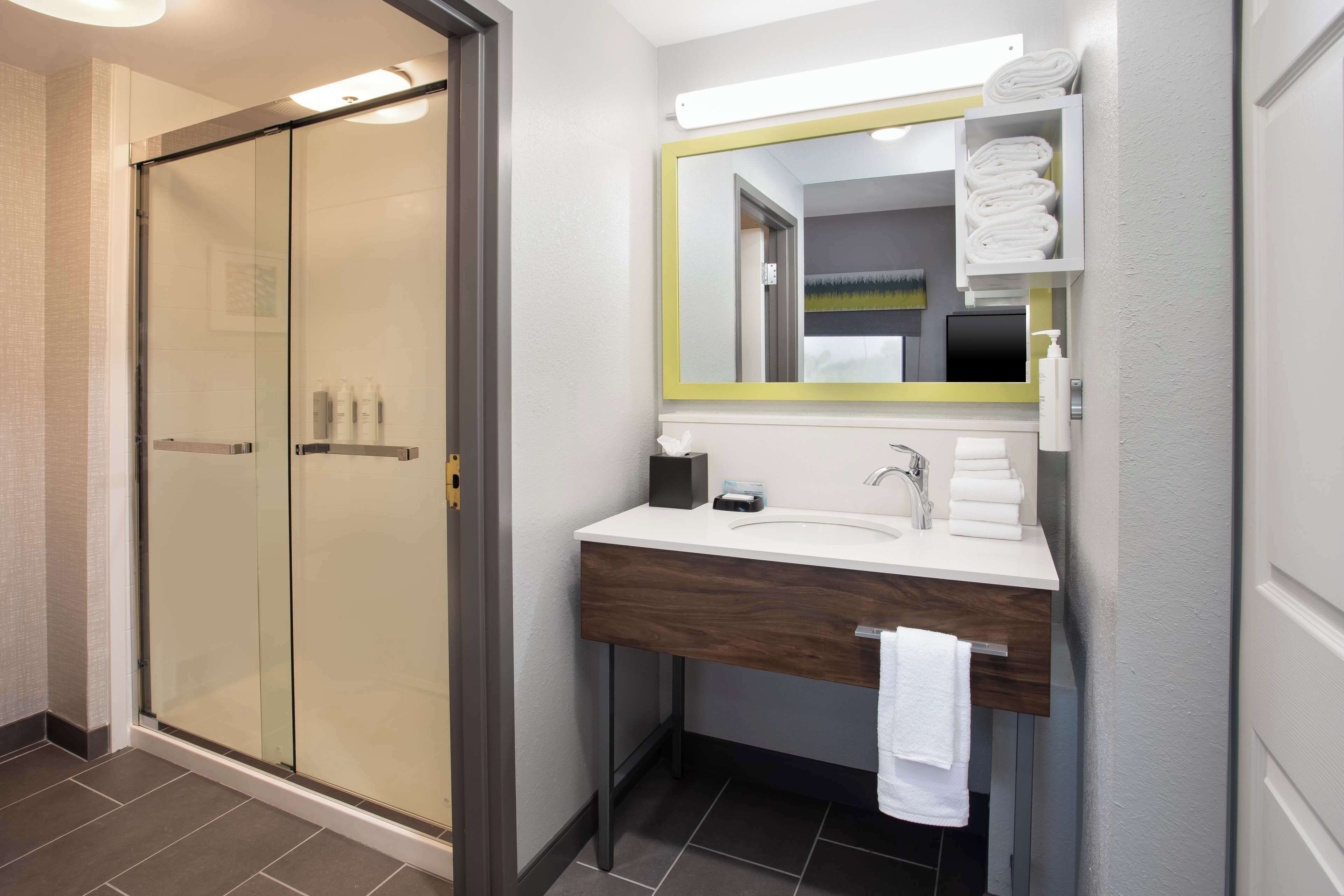 A modern bathroom with a glass shower enclosure, a wooden vanity with a mirror, and neatly folded towels.