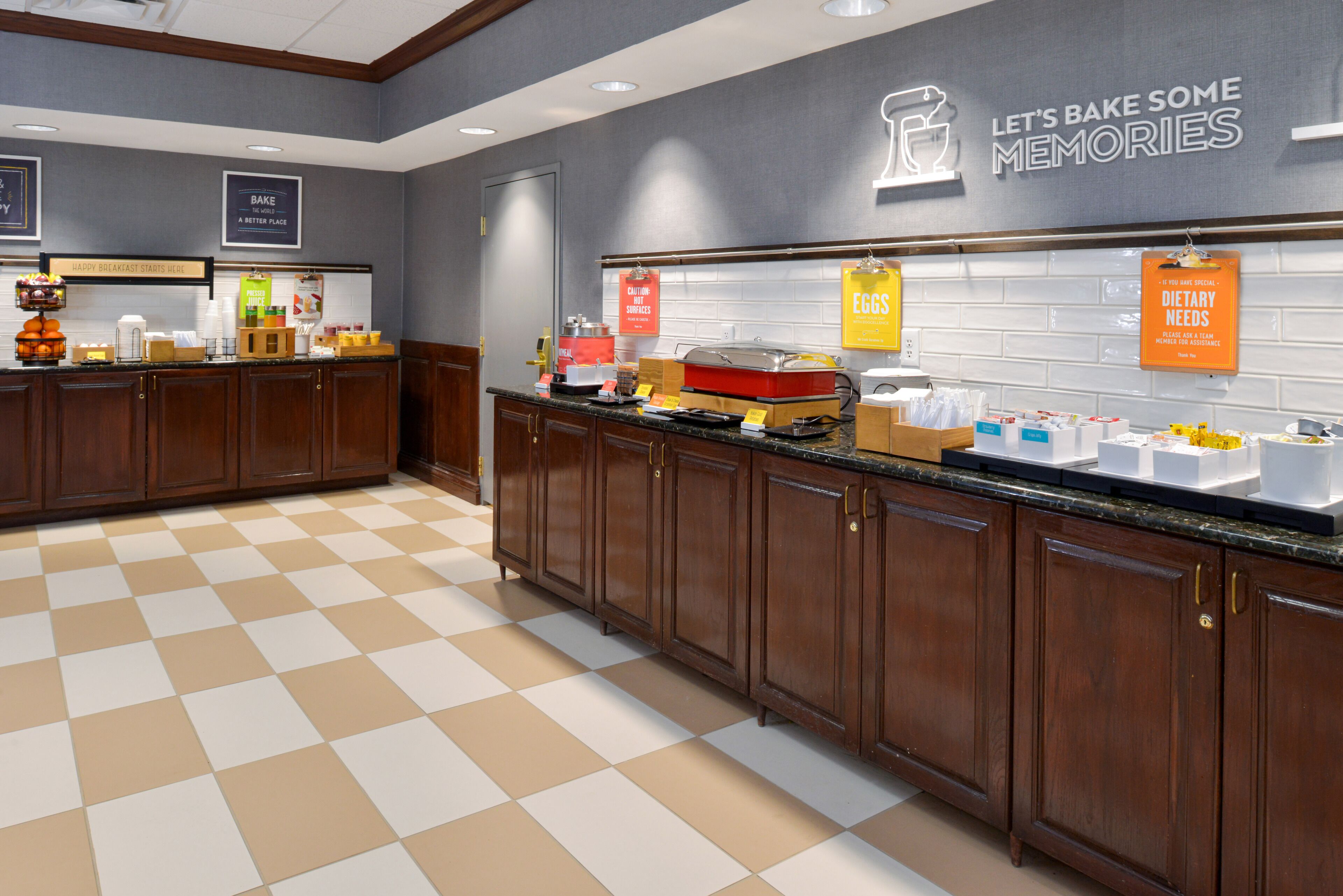 A kitchen area with wooden cabinets, a checkered floor, and various food items displayed on the counter.