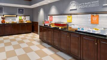 A kitchen area with wooden cabinets, a checkered floor, and various food items displayed on the counter.