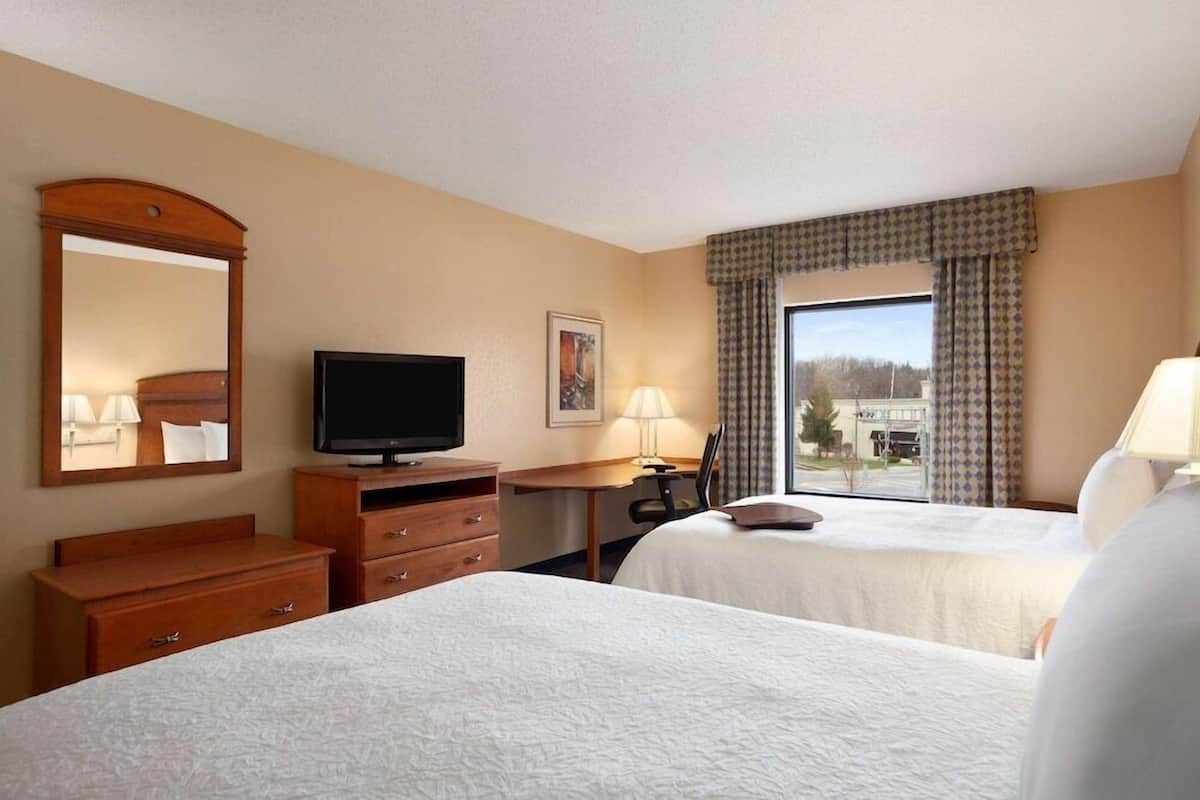 Quarto de hotel com duas camas, televisão, escrivaninha e janela com cortinas.