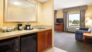 Une chambre d’hôtel équipée d’une kitchenette, d’un grand miroir, d’une télévision, d’un canapé et d’une fenêtre avec des rideaux.