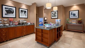 Un espace pour le petit-déjeuner à l’hôtel, aménagé en buffet, comprenant un coin café, un présentoir de fruits et divers récipients contenant de la nourriture.