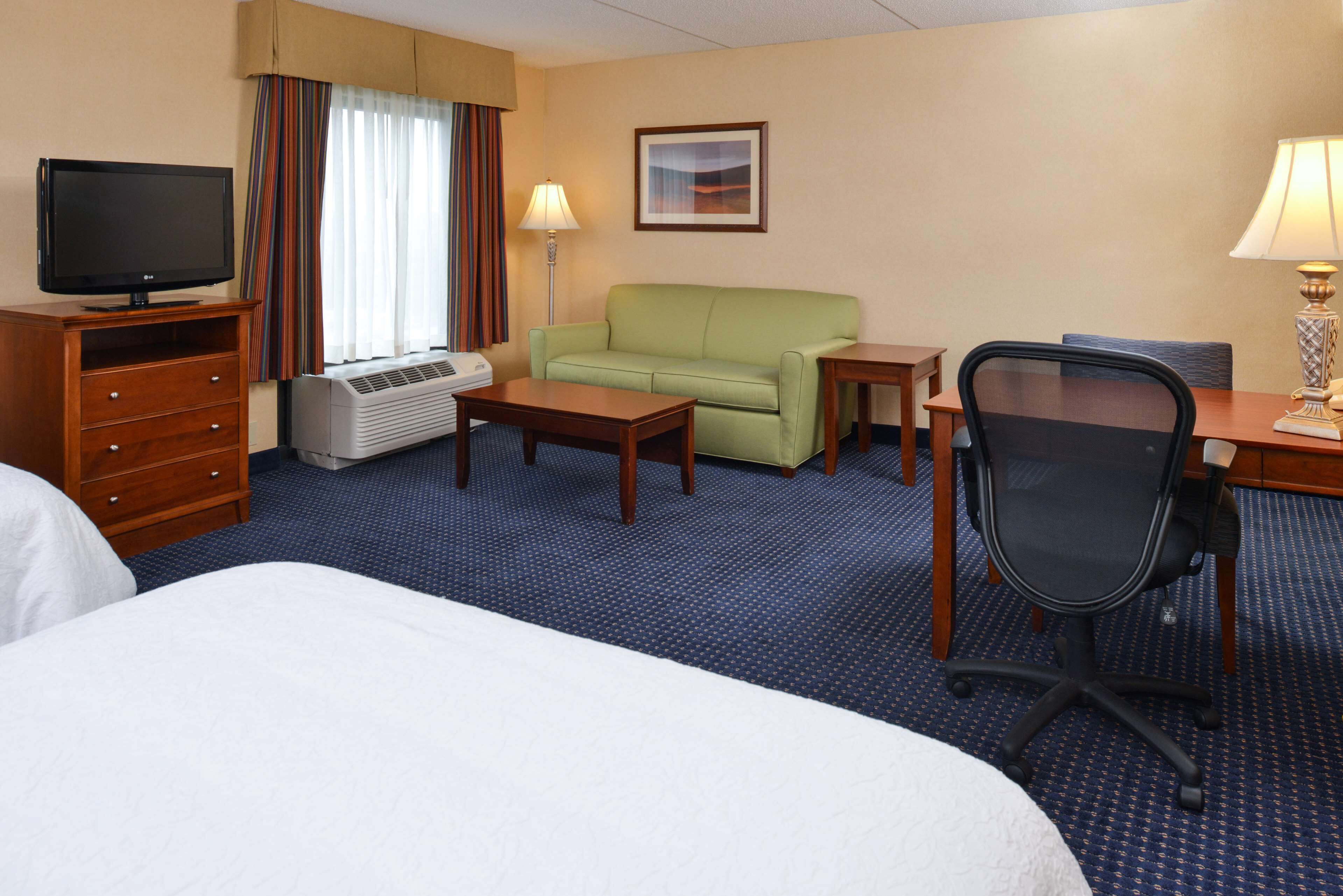 Een hotelkamer met een bed, een televisie, een groene bank, een bureau met stoel en een lamp.