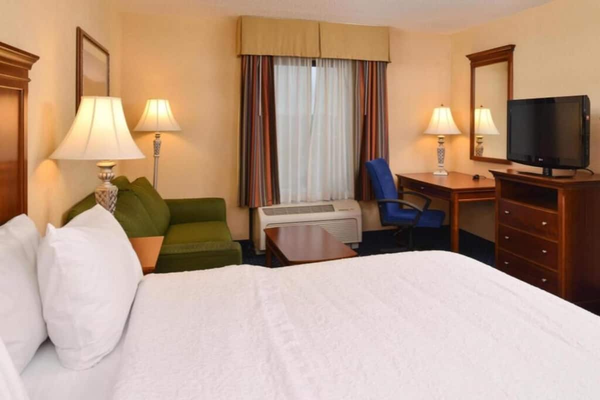 A hotel room with a bed, a desk, a chair, a television, and a window with curtains.