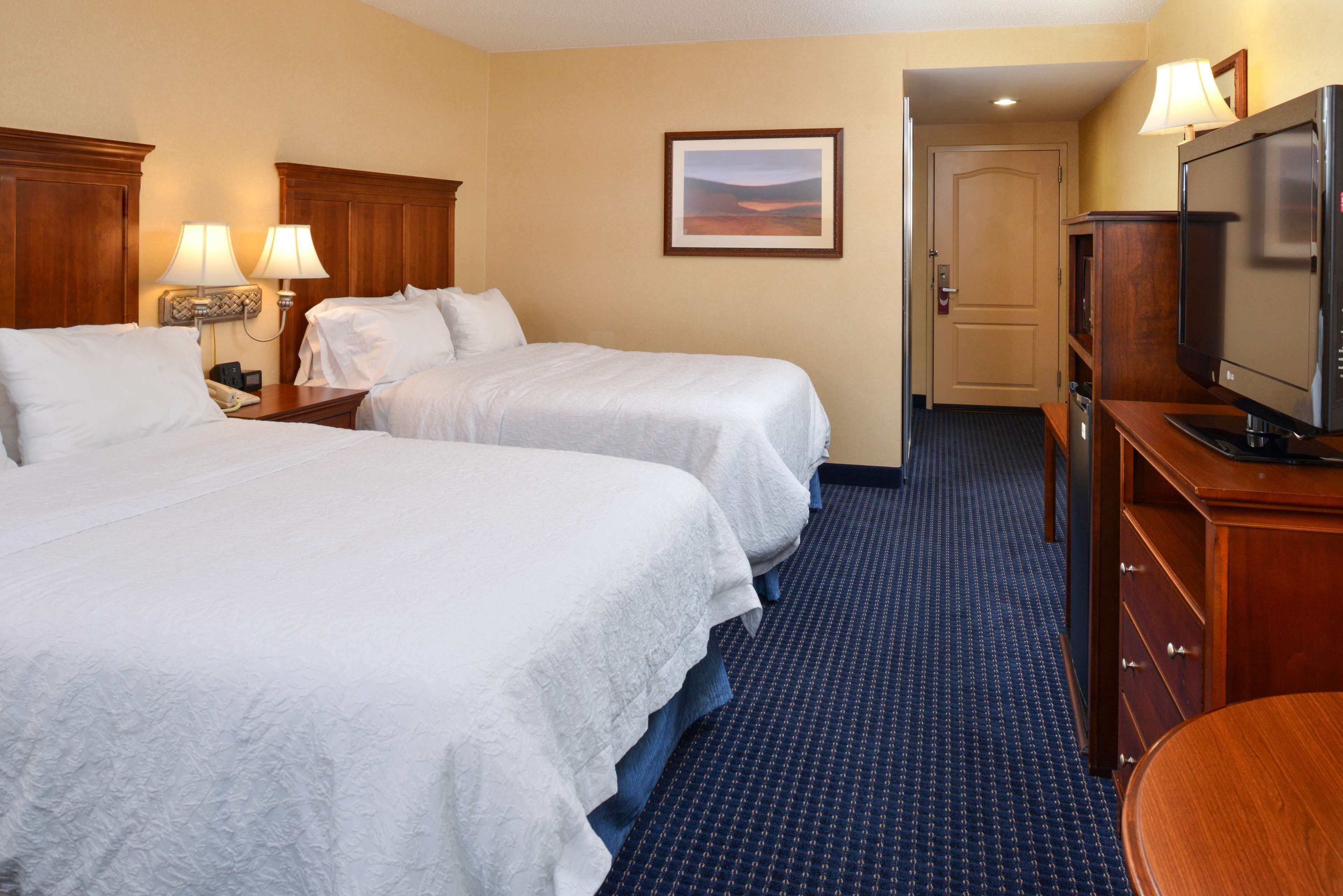 A hotel room with two beds, a television, a desk, and a door leading to another room.