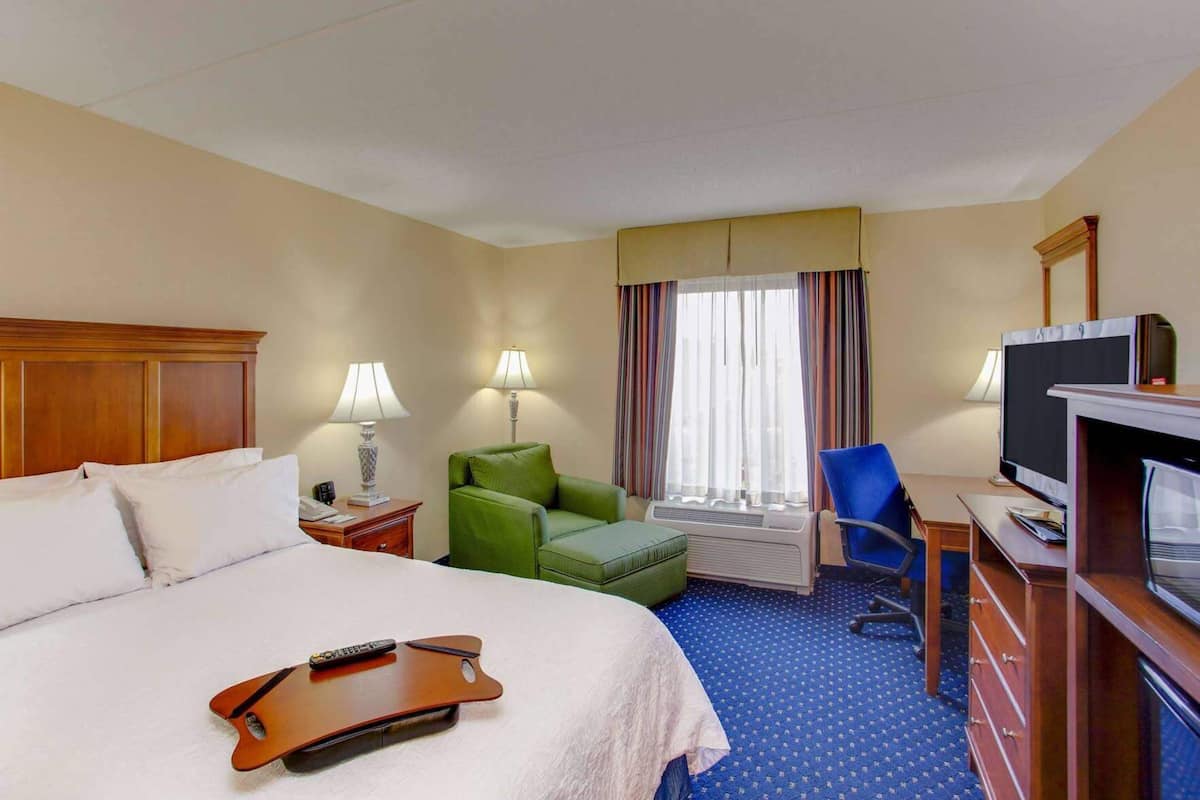 A hotel room with a bed, a desk with a computer, a television, a chair, and a window with curtains.