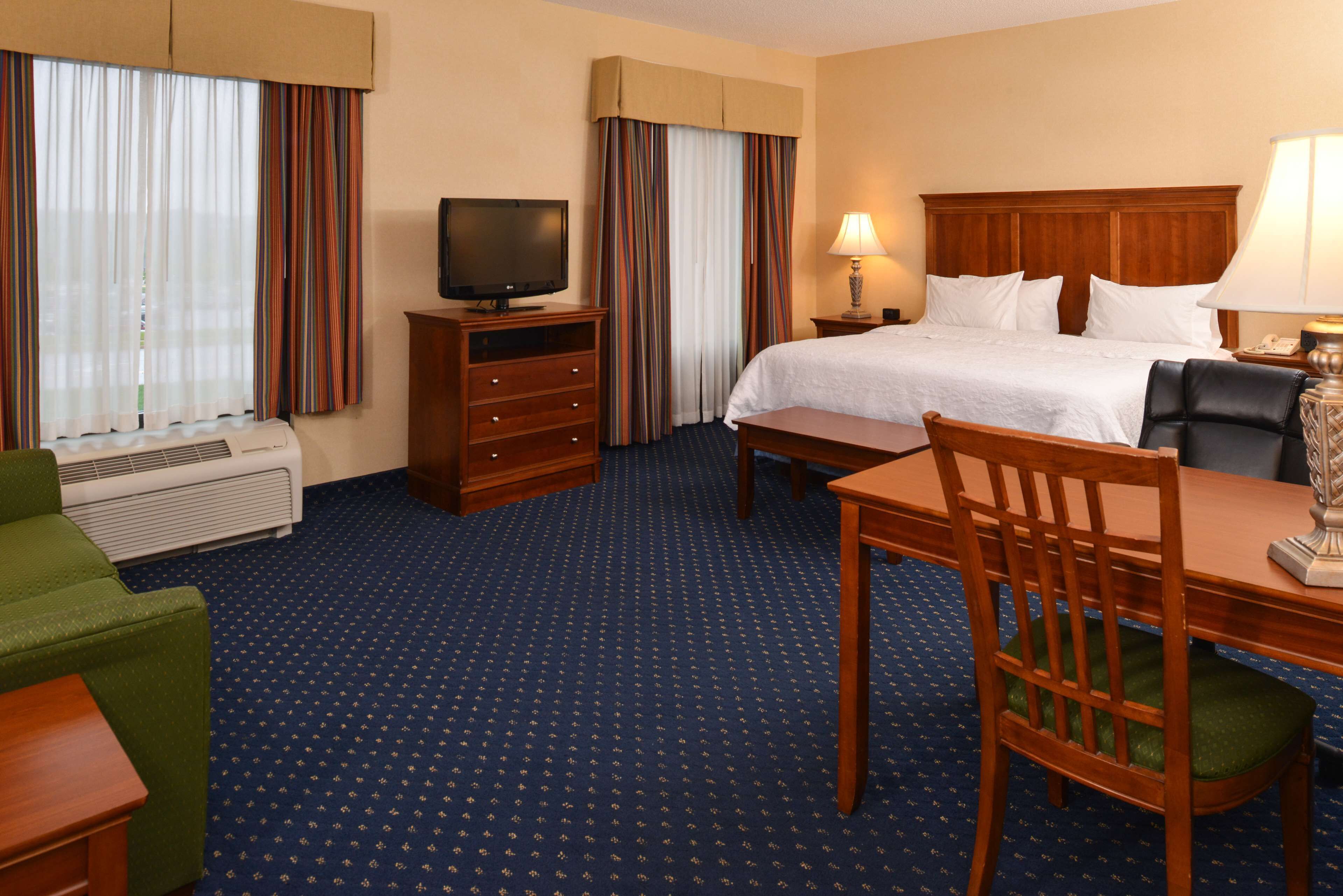 Quarto de hotel com cama, escrivaninha, cadeira, televisão, luminária e aquecedor.