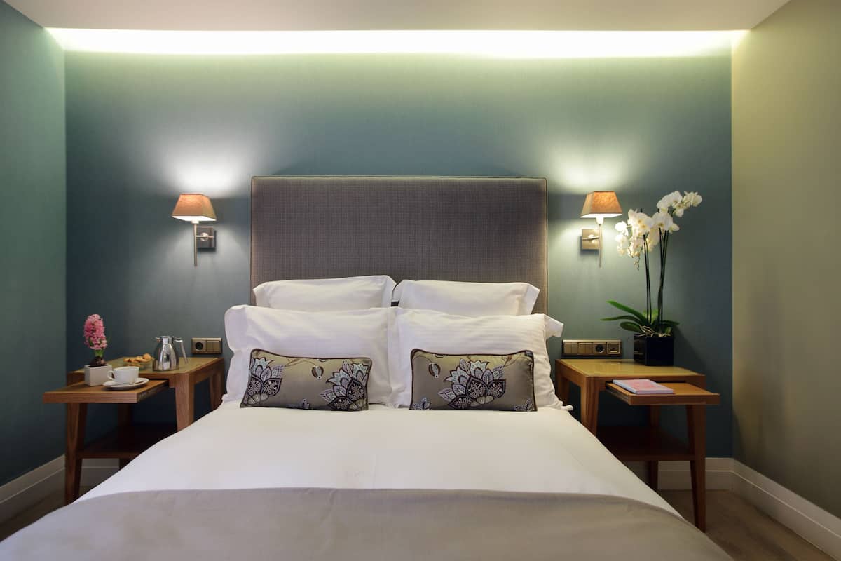 A neatly made bed with white linens and decorative pillows, flanked by two bedside tables with lamps and a potted plant.