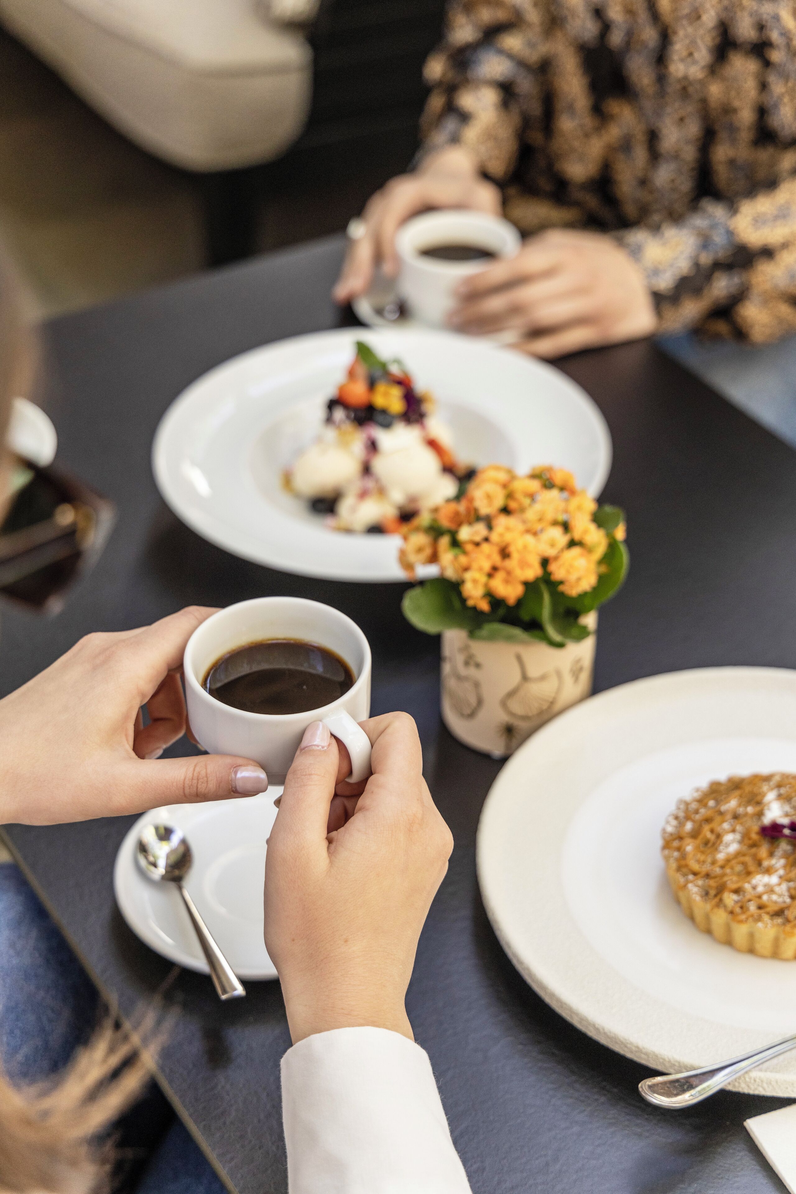 A dining table with a cup of coffee, a dessert plate, and a small potted plant.