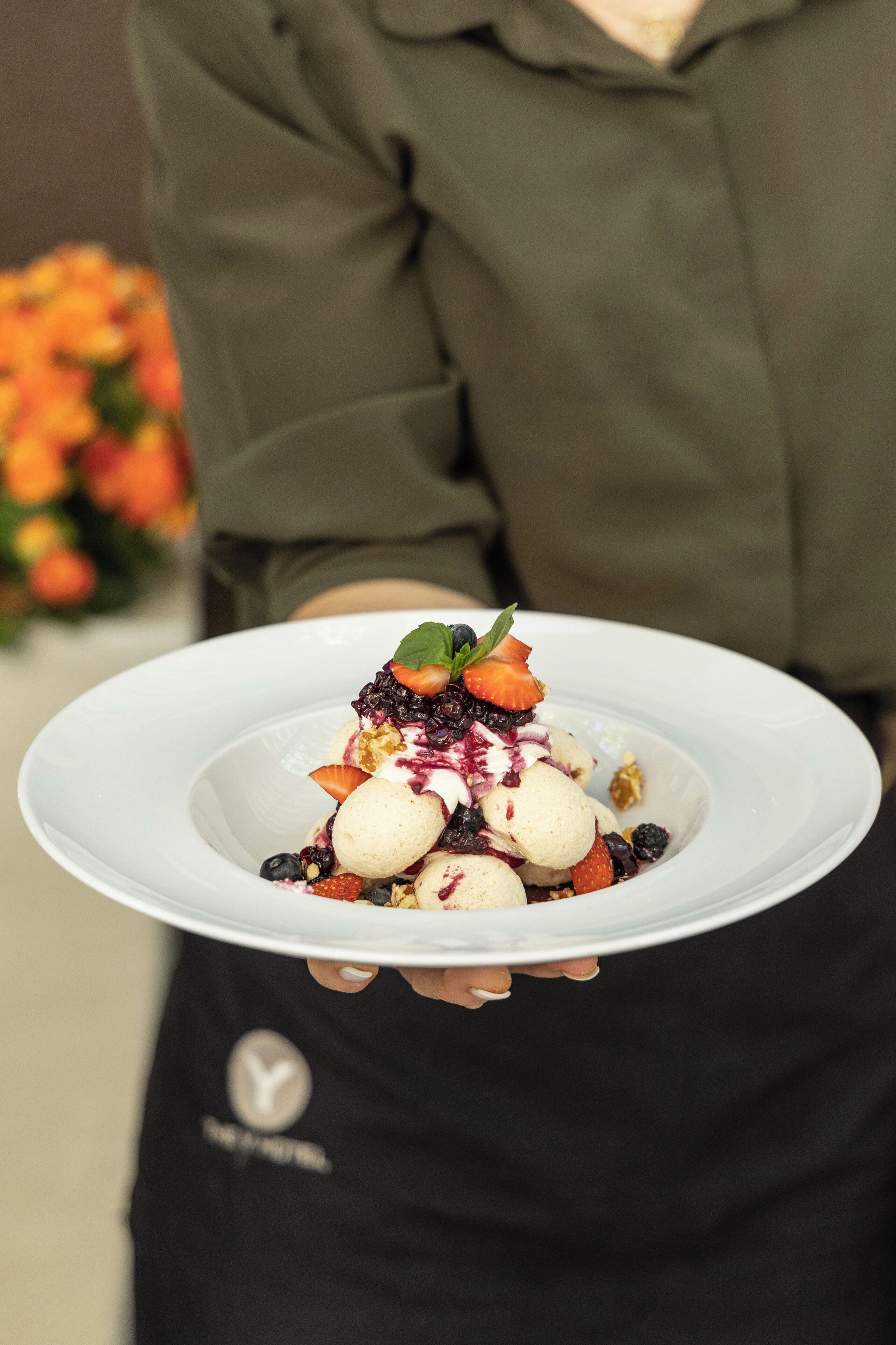 A person holding a white plate with a dessert that includes ice cream, berries, and a mint leaf.