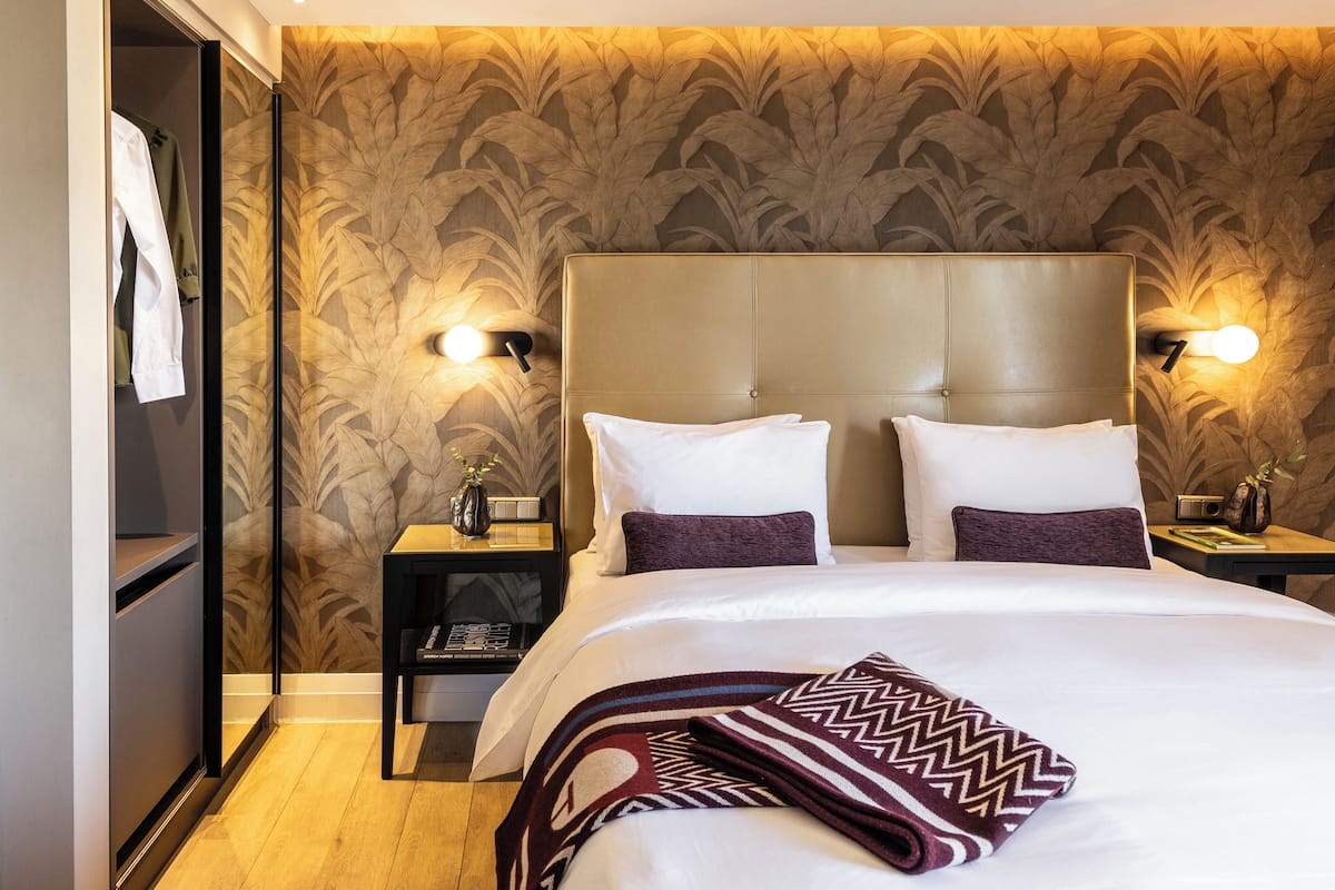 A hotel room with a large bed, two nightstands, a wardrobe, and a patterned wallpaper.