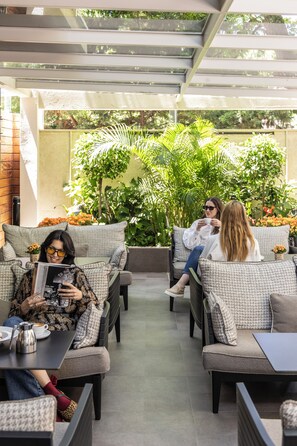 An outdoor seating area with wicker furniture, a coffee table, and a potted plant. - The Y Hotel (Kifisia)