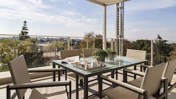 Een glazen tafel met stoelen op een balkon met uitzicht op een stadsbeeld.