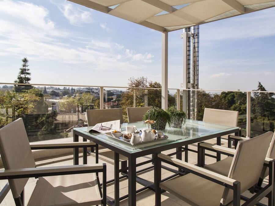 Een glazen tafel met stoelen op een balkon met uitzicht op een stadsbeeld.