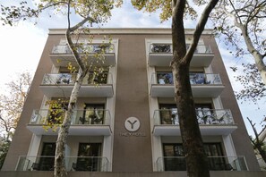 A multi-story hotel with balconies, a central logo, and a tree in the foreground. - The Y Hotel (Kifisia)