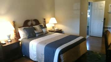 A neatly made bed with a headboard, two bedside tables with lamps, and a door leading to another room.