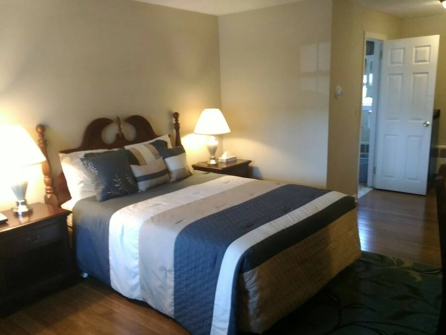 A neatly made bed with a headboard, two bedside tables with lamps, and a door leading to another room.