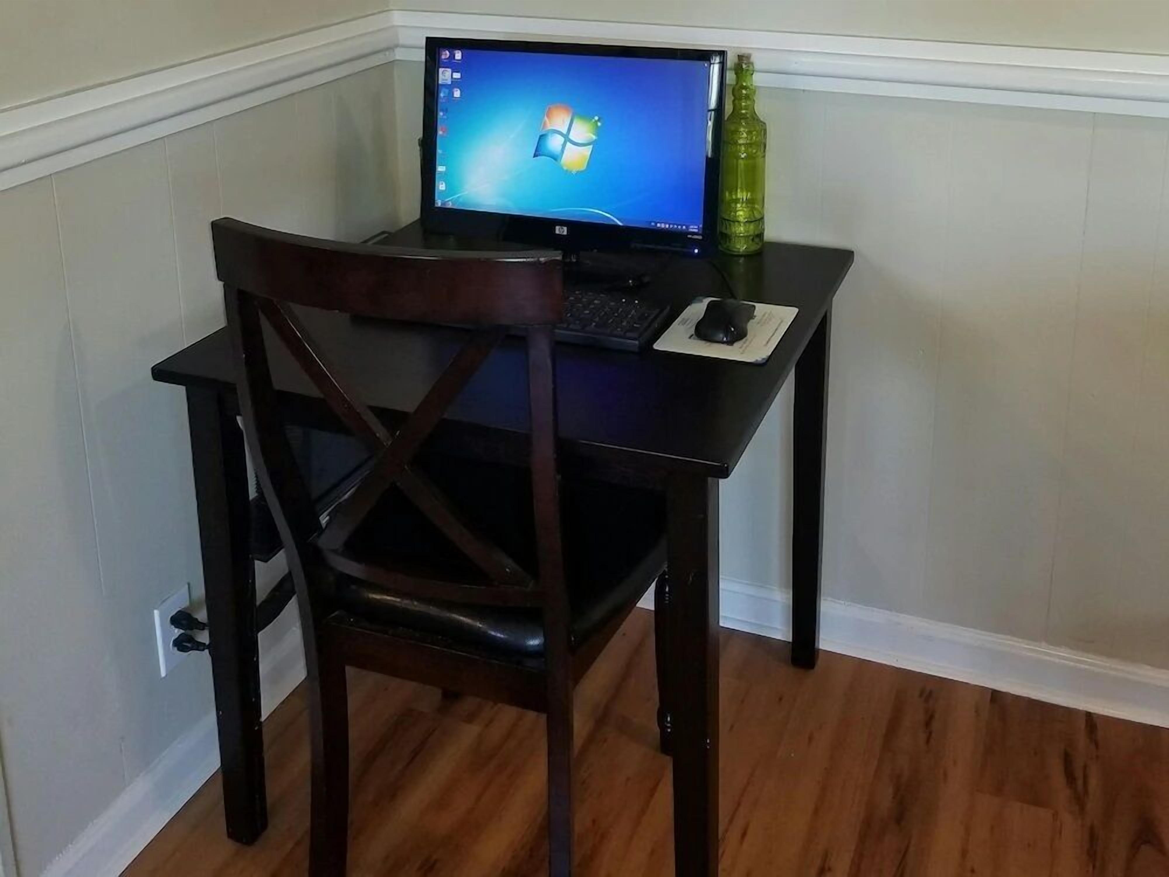 Escritorio en esquina con una computadora portátil, un ratón y una botella verde.
