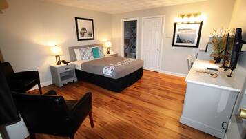 A hotel room with a bed, bedside tables, a desk, a chair, and a television.