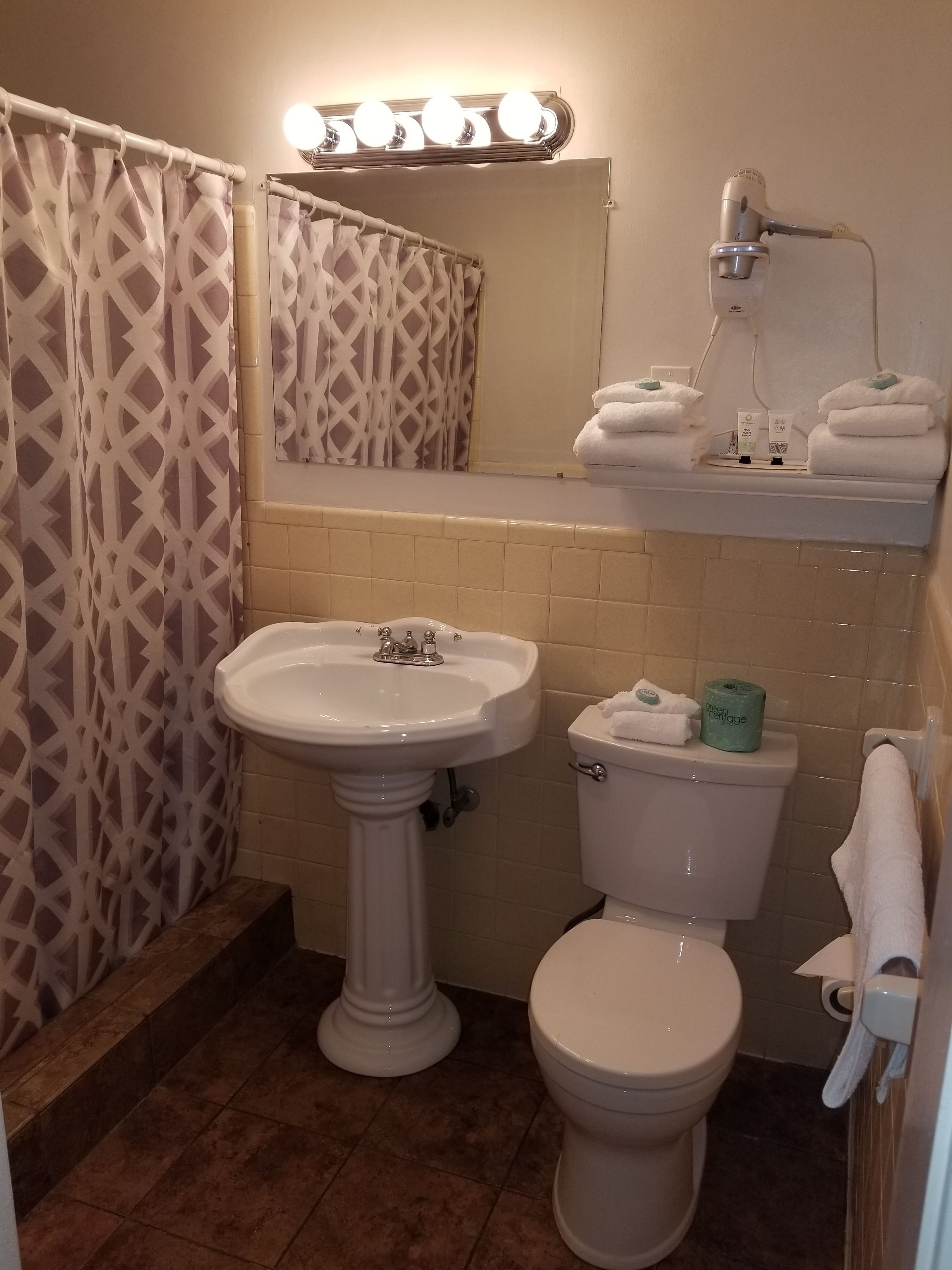 A bathroom with a pedestal sink, toilet, and a vanity with a mirror and lights.
