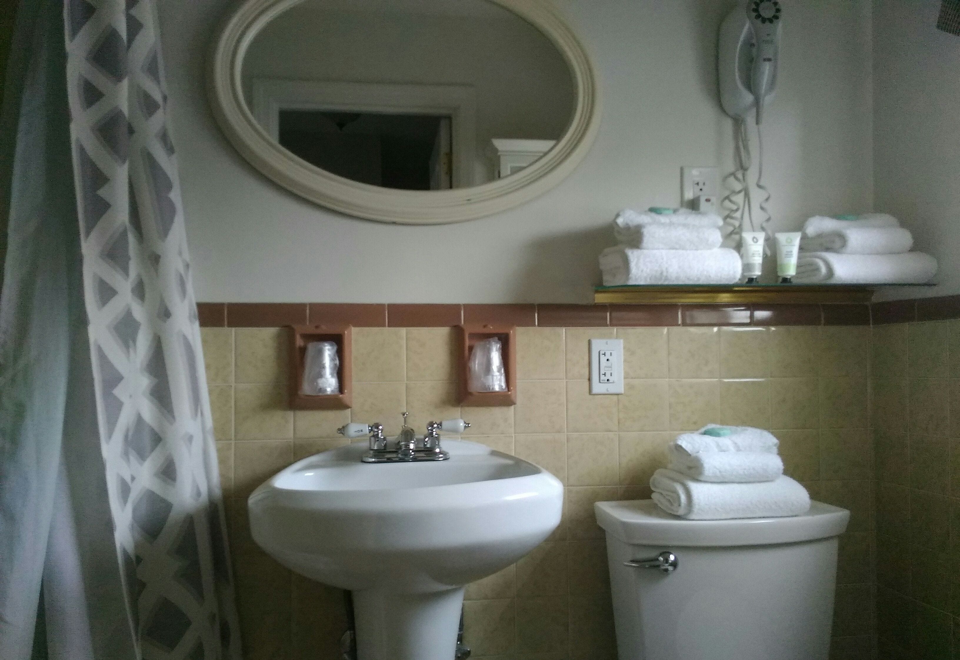 Un baño con lavamanos, inodoro y espejo. Hay toallas y artículos de aseo en la encimera.